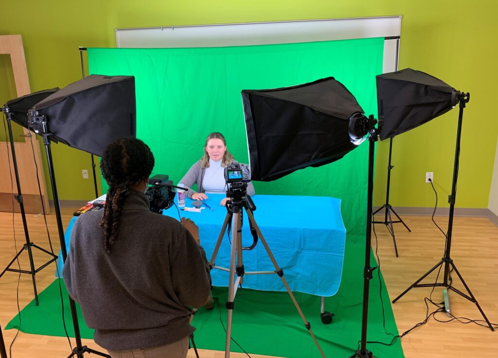 person sitting in front of green screen being filmed