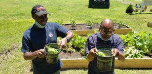 Two people outside in garden holding baskets of veggies