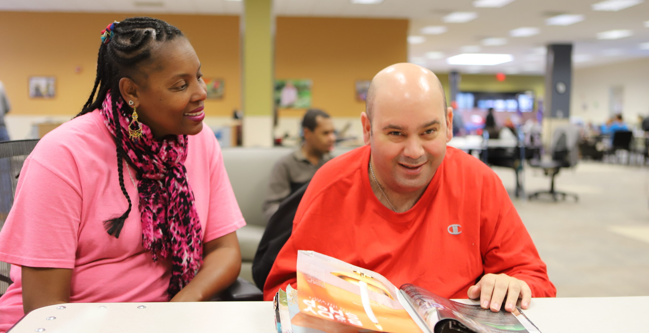 Man with hands in magazine looking at camera next to person