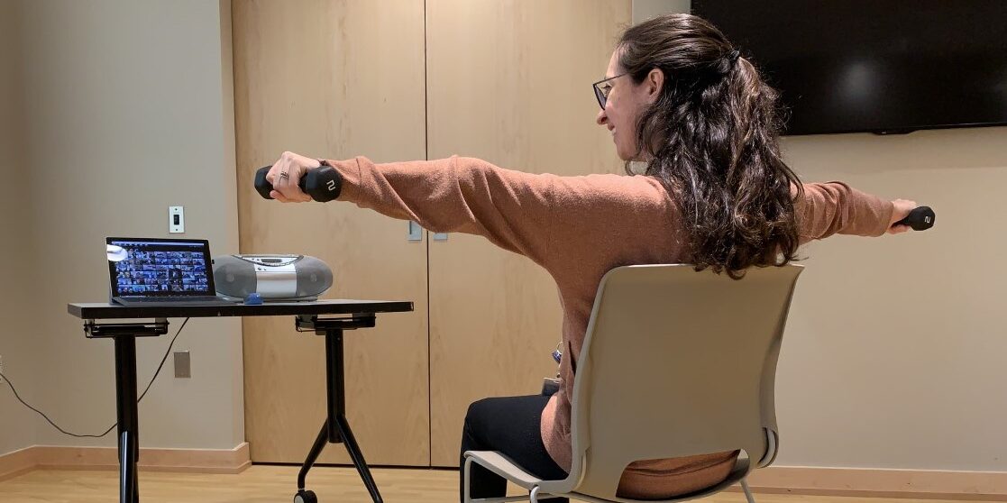 Woman looking at computer screen with weights in hand
