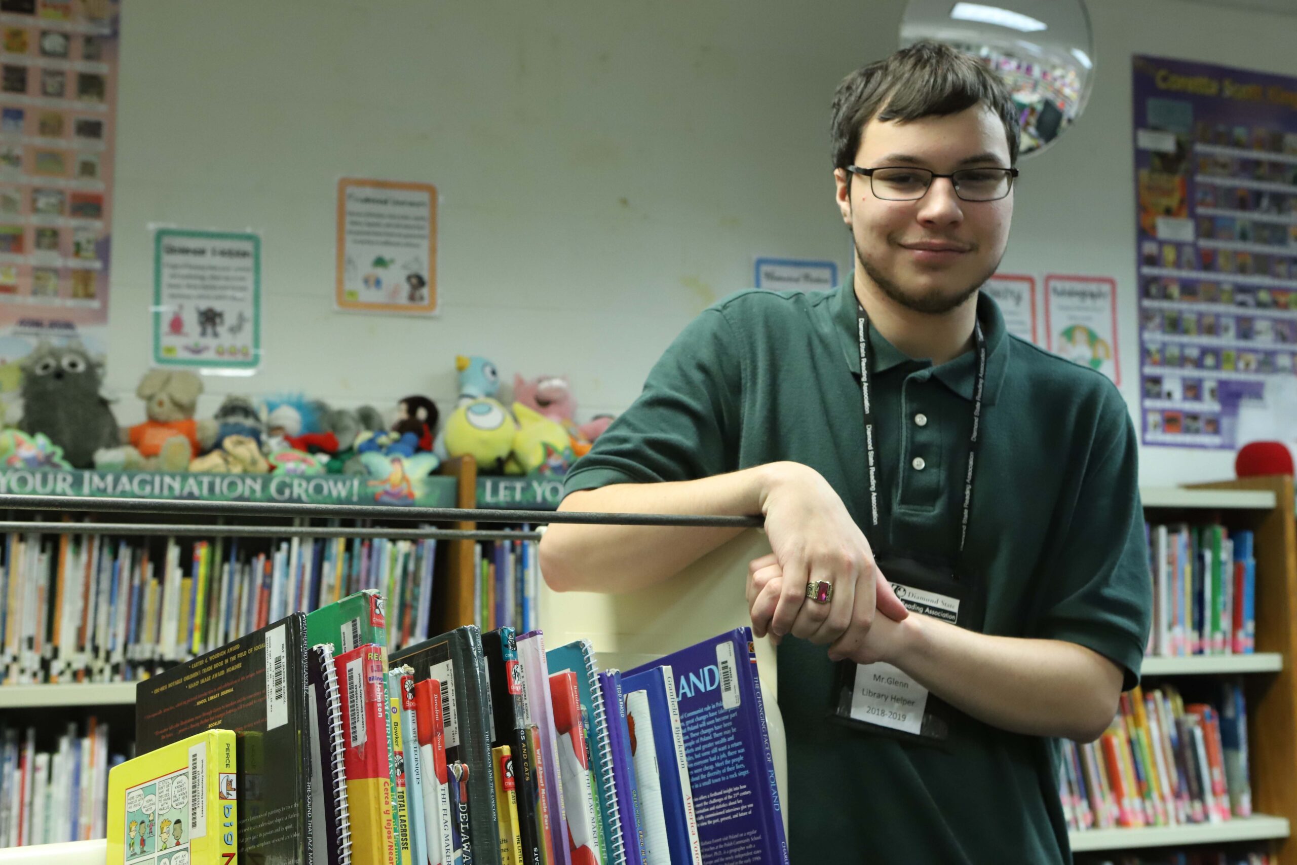 man leaning on shelf of books smiling at camera