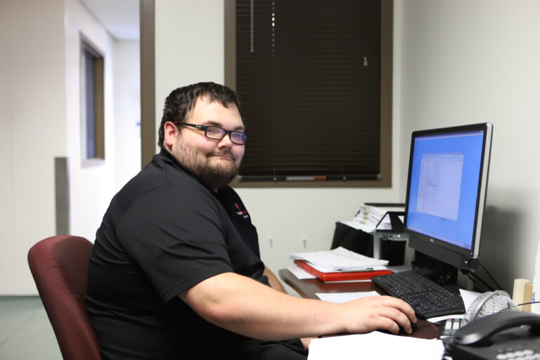 man smiling at camera sitting in front of computer