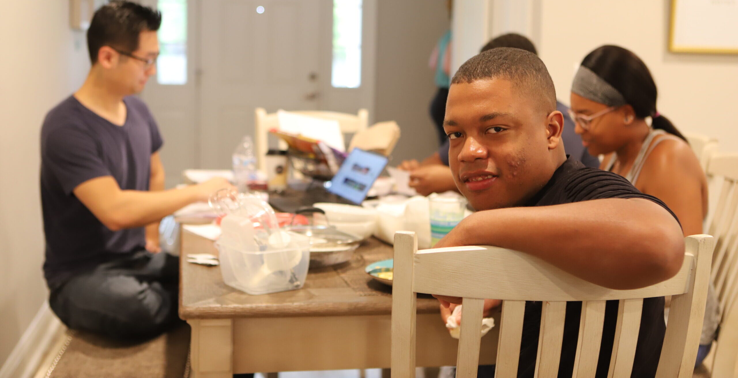 man looking back at camera while sitting at table surrounded by other people
