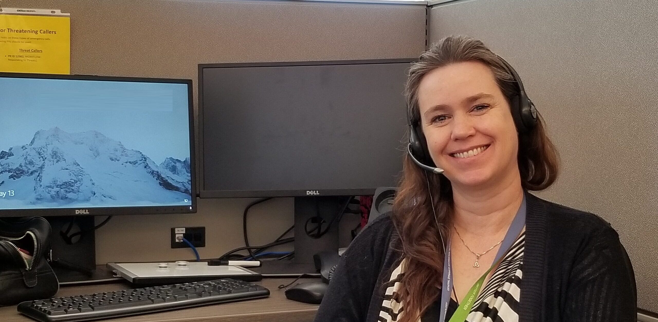 Woman with headshot smiling at camera in front of computer