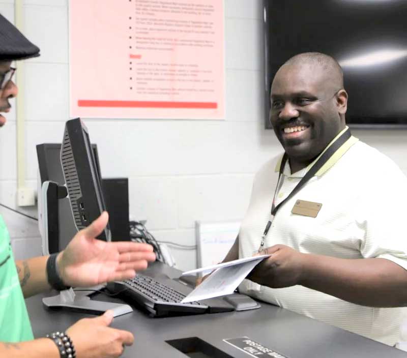 man handing another person piece of mail from behind desk