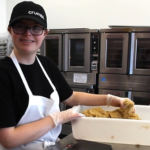 person smiling at camera with hands in dough