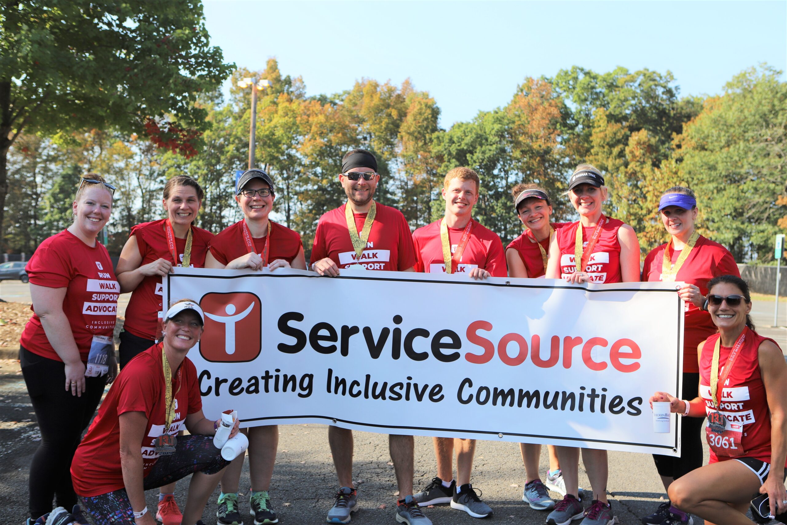 group of people holding up large banner that says ServiceSource Creating Inclusive Communities