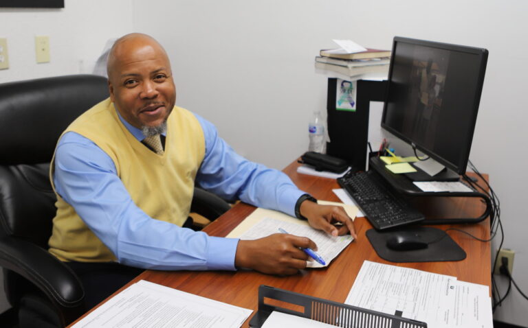 man sitting at office desk smiling at camera