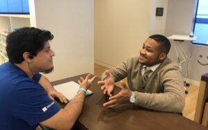 two young adults talk while sitting across from each other at table