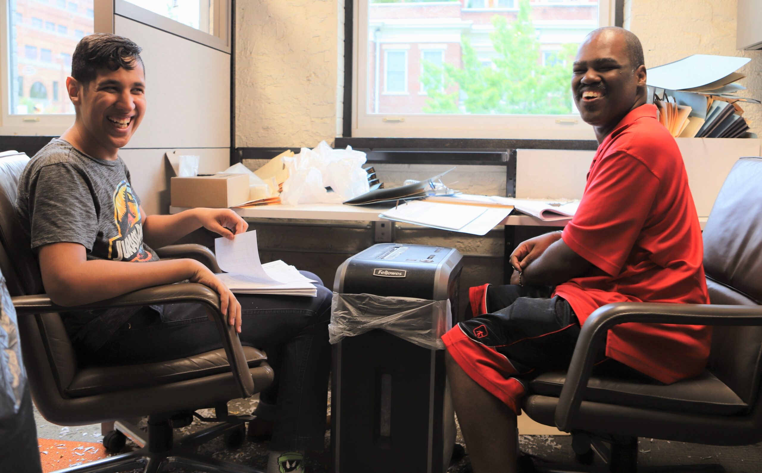 two people sitting down in front of paper shredders