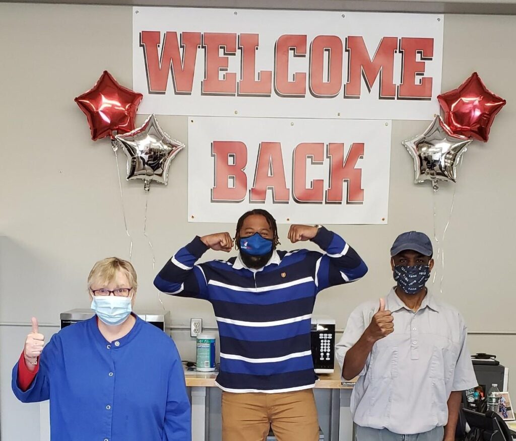 three people in front of welcome sign in masks