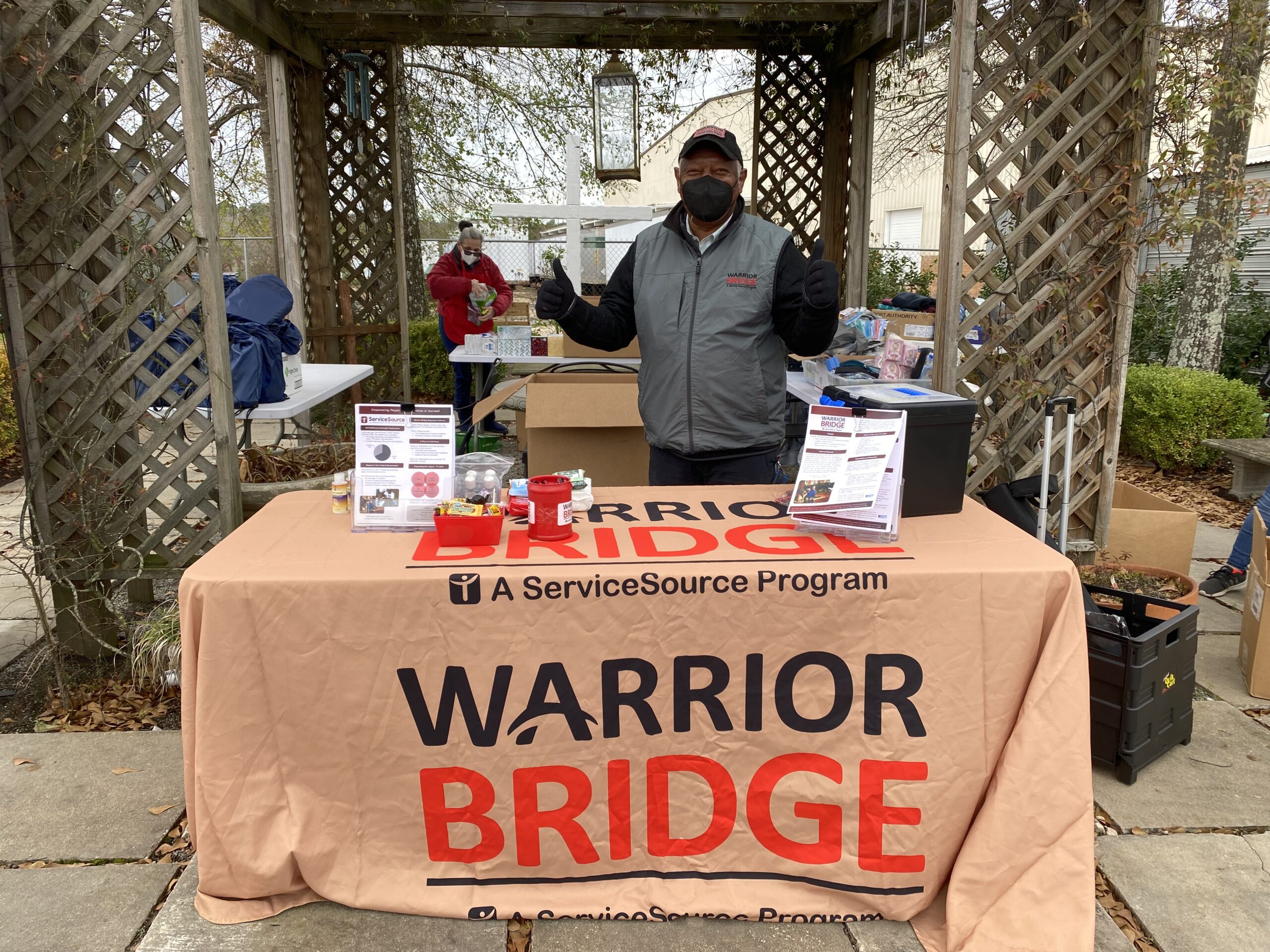 Person standing in front of table with Warrior Bridge logo