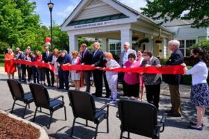 Group of people cutting red ribbon with large scissors